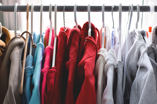Clothes rack with hoodies organized by colour on hangers closeup