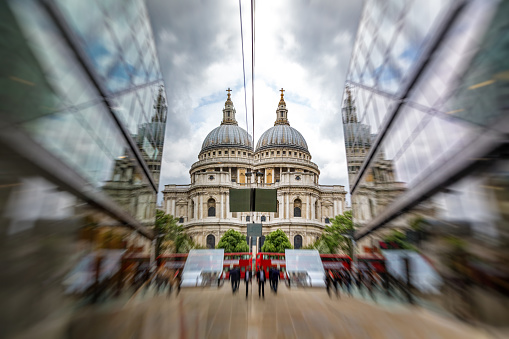 St Paul's Cathedral reflected in modern glass buildings, with red London buses and people waling by. Focus on the Cathedral with zoom blur.