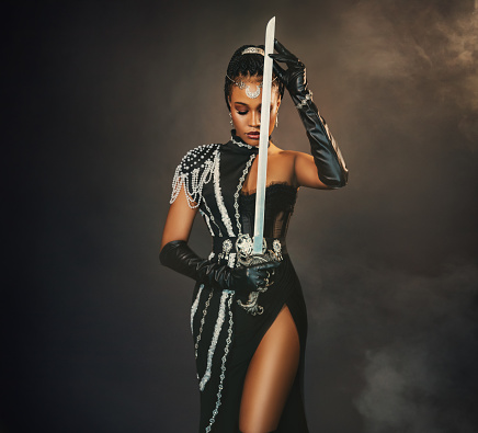 Portrait fantasy african american woman warrior holding sword weapon in hand. Dark queen girl in black military dress costume. Gothic lady elf fairy. Sexy beauty face fashion model pray. Studio photo.