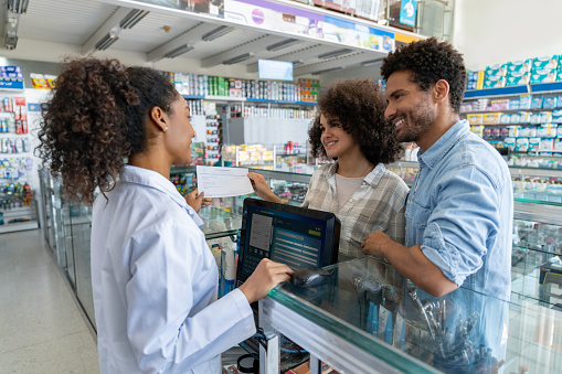 Happy Latin American couple buying prescription medicines at the pharmacy and talking to the retail clerk