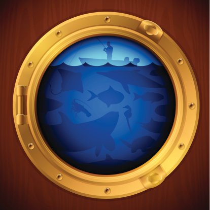 A porthole looking out on a man fishing and ocean life. 