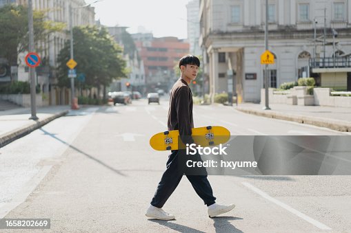 istock Young asian skateboarder walking on the street 1658202669
