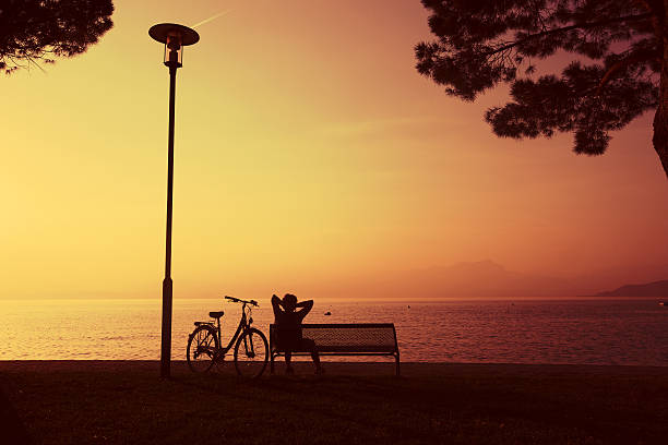 Woman cyclist on seashore bench at sunset
