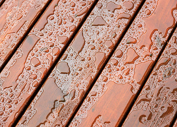 Wet Outdoor Decking Surface Close-up on the wet surface of protected wooden decking following heavy rain. wood stain stock pictures, royalty-free photos & images