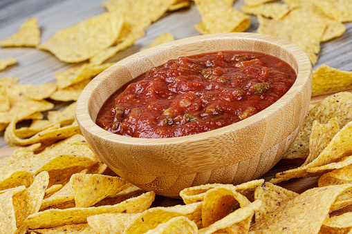 A large wooden bowl of delicious Salsa and Roasted Corn Tortilla or Nacho Chips on a wooden background with copy space
