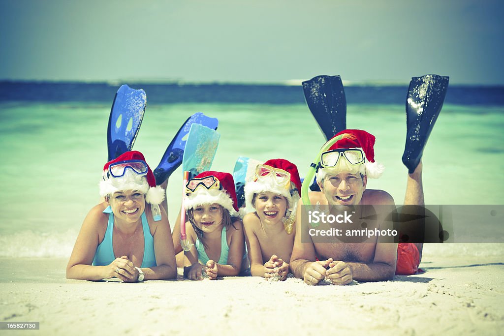 vintage postcard family beach vintage image of happy family with santa hats and snorkeling gear relaxing on sandy beach in front of tropical lagoon Beach Stock Photo