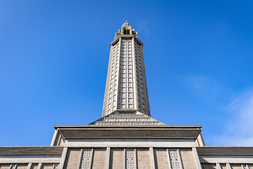 St. Joseph's Church (Eglise St. Joseph) in downtown Le Havre City from below against blue summer sky. St. Joseph's Church in Le Havre is a Roman Catholic Church built between 1951 and 1957 as part of this reconstruction of Le Havre City, it acts as a memorial to the five thousand civilians fallen in World War II. The church tower is 107 meters tall and acts as a beacon visible from out at sea. Le Havre, Normandy, France, Europe.