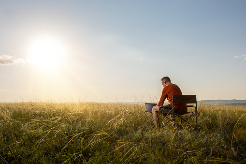 man reading an email on a laptop with 5g internet while working by summer nature at sunset. remote work.