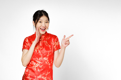 Happy Asian woman wearing traditional cheongsam qipao dress hand pointing up to copy space isolated on white background. Happy Chinese new year.