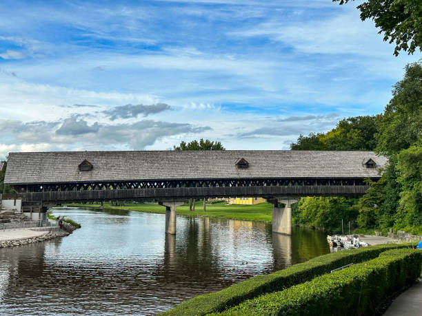 This beautiful wood covered bridge spans 239 feet across the Cass River in Frankenmuth, Michigan. It has a 19th century design although it was completed in 1980. There is a vibrant blue sky with white clouds above this bridge.
