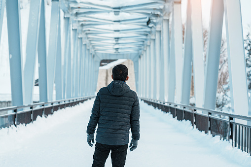 man tourist Visiting in Biei, Traveler in Sweater sightseeing Shirahige Waterfall bridge with Snow in winter. landmark and popular for attractions in Hokkaido, Japan. Travel and Vacation concept