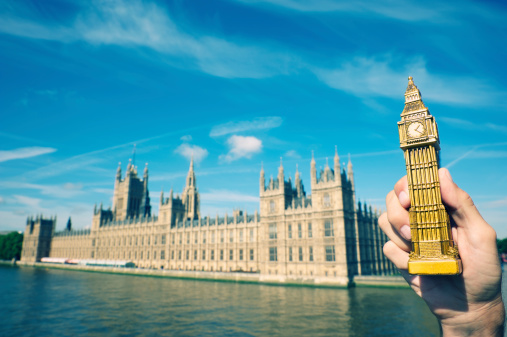Hand holds a plastic souvenir Big Ben in sunny London skies next to Houses of Parliament