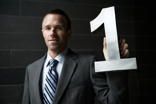 Businessman holds a shiny number one up against a conservative dark background