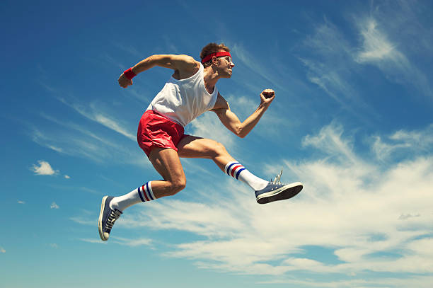 Nerd Athlete Hurdle Jumps Blue Sky Nerd athlete in headband and 70s socks leaps against blue sky hurdling track event stock pictures, royalty-free photos & images