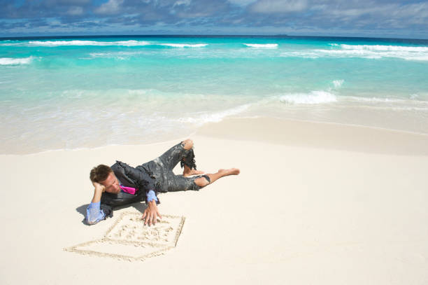 Castaway businessman in ripped suit lies on tropical beach using a laptop computer drawn in the sand