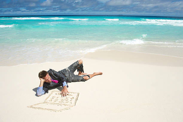 Castaway Businessman Lies on Beach Using Sand Laptop Castaway businessman in ripped suit lies on tropical beach using a laptop computer drawn in the sand castaway stock pictures, royalty-free photos & images