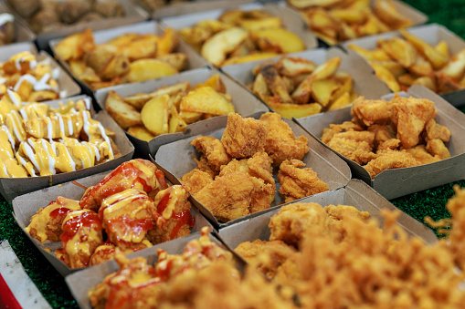 Various choices of deep-fried chicken, potato wedges, and enoki mushrooms are displayed on a paper plate at a Malaysian night market stall
