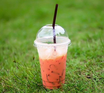 a photography of a plastic cup with a straw and a drink in it, wax light orange drink in a plastic cup with a straw.
