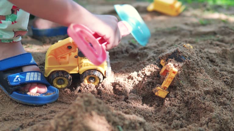 Asian boy plays and digs sand using a toy digger and dump truck.