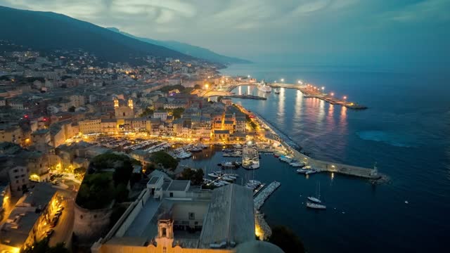 Aerial view of Bastia harbor and old town, ferry leaves the port, mediterranean sea, Corsica, France. Flying over evening Bastia with city lights, Corsica island