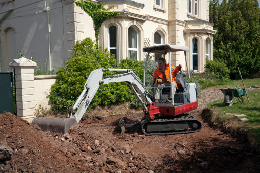 Mini digger in front of victorian house excavating in readiness for new concrete driveway. Focus on arm of digger
