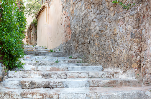 Traditional narrow stone stair, stonewall building, green plant on wall destination for vacation Greece. Empty worn stairway from down to upper.