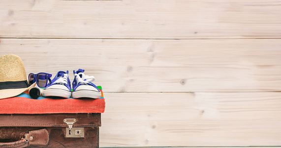 Summer vacation preparation on white wooden background. Vintage suitcase, sunglass, towel, hat, sneaker. Ready for beach. Copy space