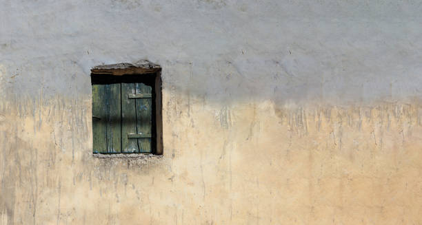 istock Aged wooden closed shutter on faded worn empty stonewall facade background, sunny day. Copy space 1658507291