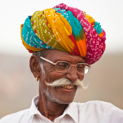 Senior Indian in colorful Turban and glasses smiling. He is a camel owner at Pushkar camel fair.