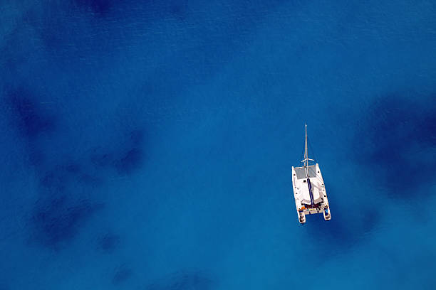 Sailing ship on an ocean of blue Sailing ship anchored in a bay with beautiful sea color. Shot from above. catamaran sailing boats stock pictures, royalty-free photos & images