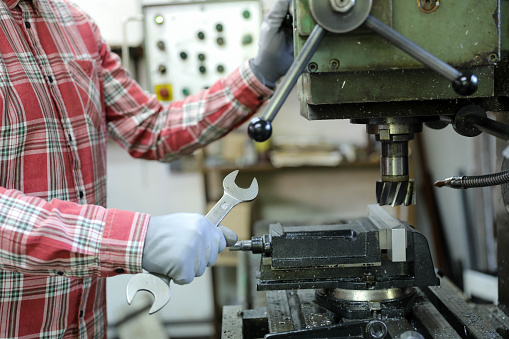 Worker in uniform operating in manual lathe in metal industry factory.