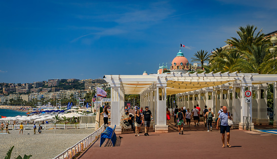 Nice, France - May 23, 2019: People on famous Promenade des Anglais with Mediterranean Sea coastline and Negresco hotel in the background, Cote d'Azur