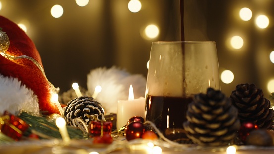 I pour hot chocolate, against the background of a garland of lights. Christmas table with candles and decorations.