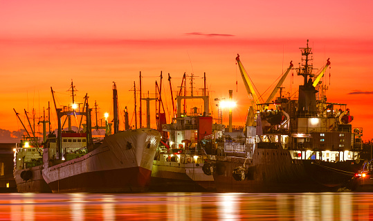 Group of fishing boats and oil tanker ship dock at harbor in industrial riverside area against beautiful dramatic twilight sky background
