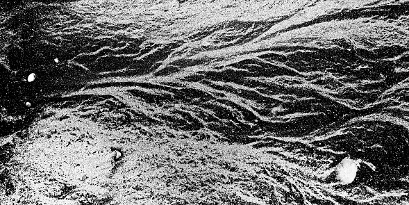 Background: nature's art graphic resource. Light and dark coloured sands on a beach in low key black and white. Looks like a river delta from high up.