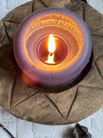Burning scented candle on a round wooden carved holder placed on a white cloth