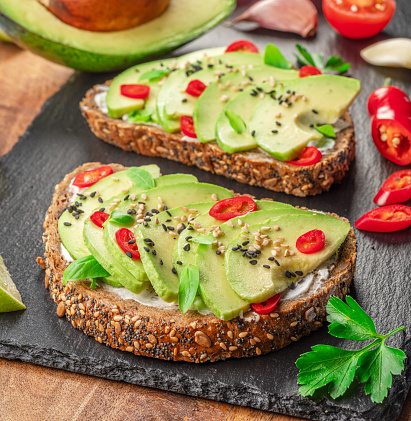 Avocado toasts - bread with avocado slices, pieces of red pepper and sesame  on black stone board.