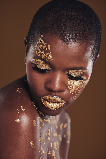 Art, facial on black woman with gold makeup and brown background, glitter paint and cosmetics. Shine, glow and African model in studio for beauty, fashion and aesthetic freedom in luxury skincare.