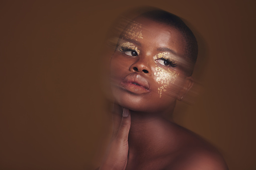 Gold beauty, blurred and black woman makeup with mockup space and cosmetics in studio. Brown background, African female model and glitter with golden shine and skin glow from facial paint sparkle