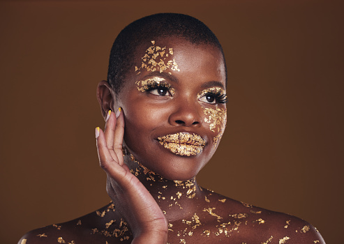 Art, paint on black woman with gold makeup and brown background, glitter on face and cosmetics. Shine, glow and African model in studio for beauty, fashion and aesthetic freedom in luxury skincare