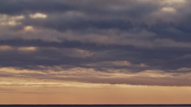 Timelapse of golden clouds moving over the ocean at dawn
