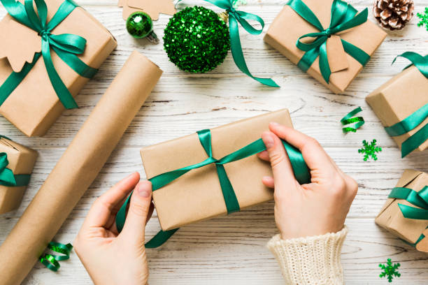 la donna sta confezionando un regalo a sorpresa per le vacanze di natale, seduta sul posto di lavoro con strumenti artigianali, vista dall'alto. regalo di natale della donna che avvolge al tavolo colorato - gift box foto e immagini stock