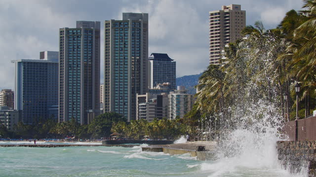 Waves splashing against sea wall with city buildings of Waikiki beach in background