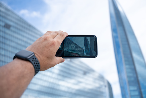 Man uses smartphone to take a picture of a modern office building, first person view