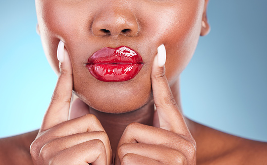 Woman, kiss and red lipstick, beauty and makeup closeup with hands on face isolated on blue background. Model, bold and  cosmetic product on lips, lipgloss and mouth with skin and shine in studio
