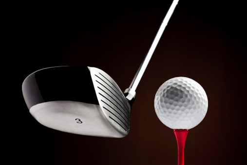 Modern golf club and a white ball on a red tee against a black background. The head shows it is a wood number three.