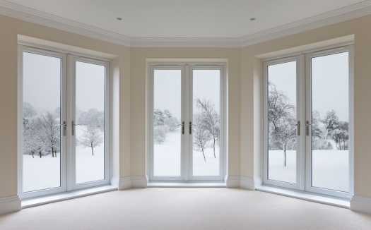 a large bay window in an expensive new home comprising high quality white double-glazed door units. View through the windows is towards a winter garden scene. This is a composition of two of my images with iStock.