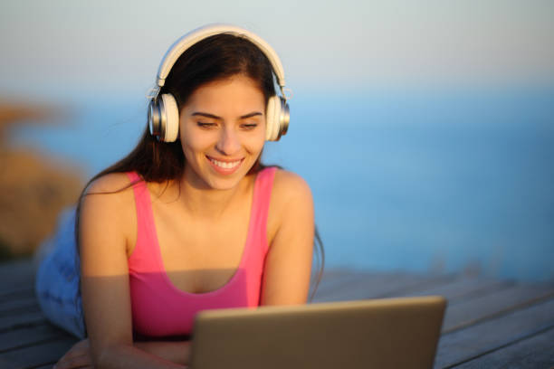 istock Happy woman with headphone using laptop on the beach 1658752387
