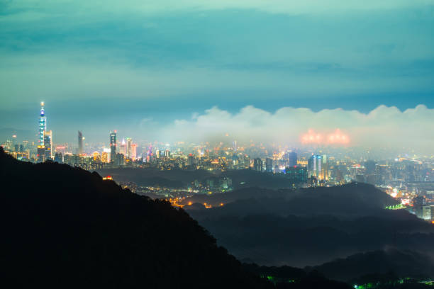 Nocturnal Marvel: City Lights and Shifting Cloudscape from the Summit. View of the urban landscape from Dajianshan Mountain, New Taipei City, Taiwan.