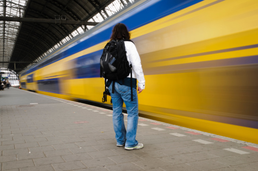 Woman is standing on the train station platform as a train speeds by at the Amsterdam Centraal Station, Holland